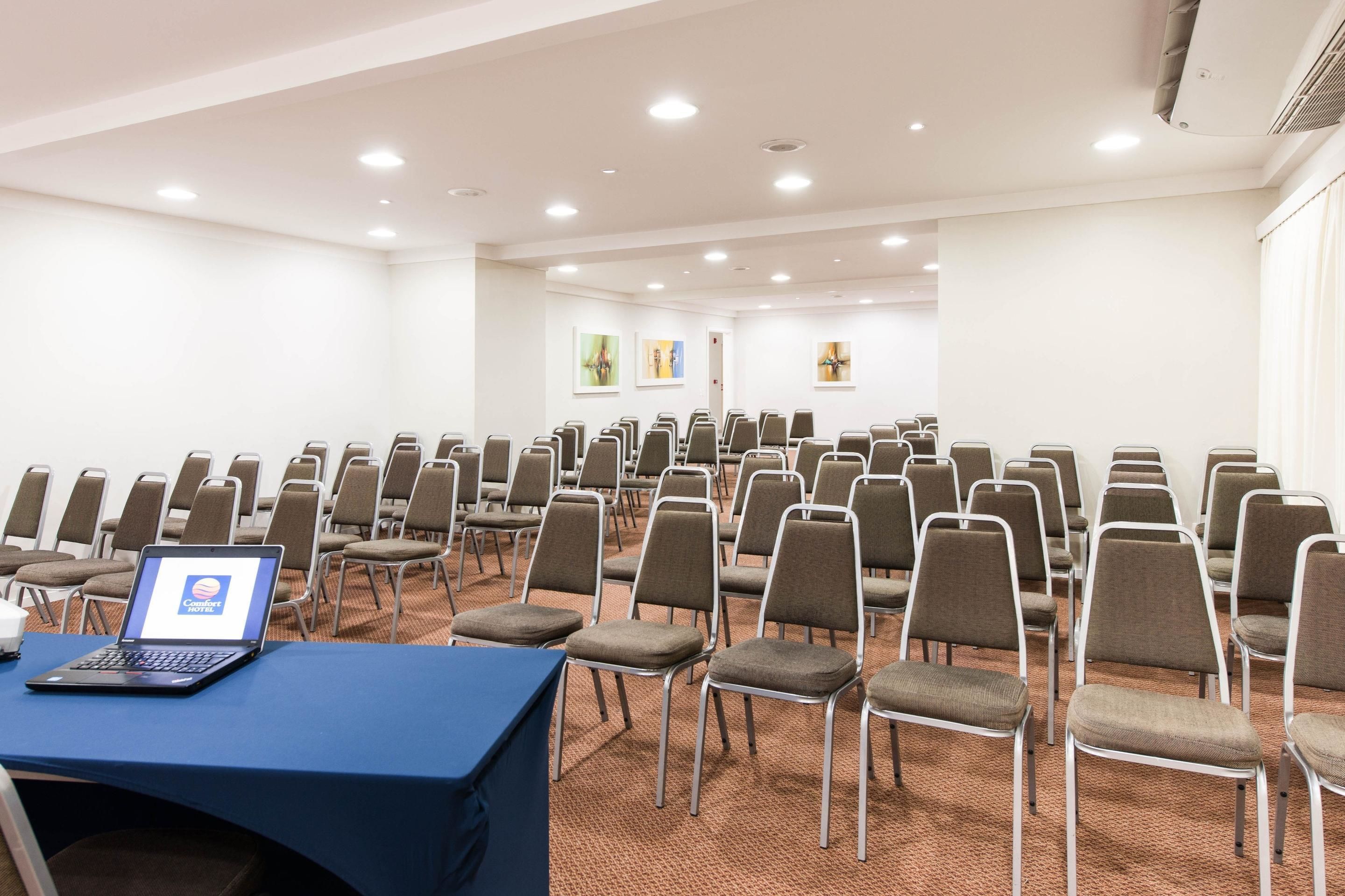 A conference room with rows of chairs, a laptop on a table, and artwork on the walls.