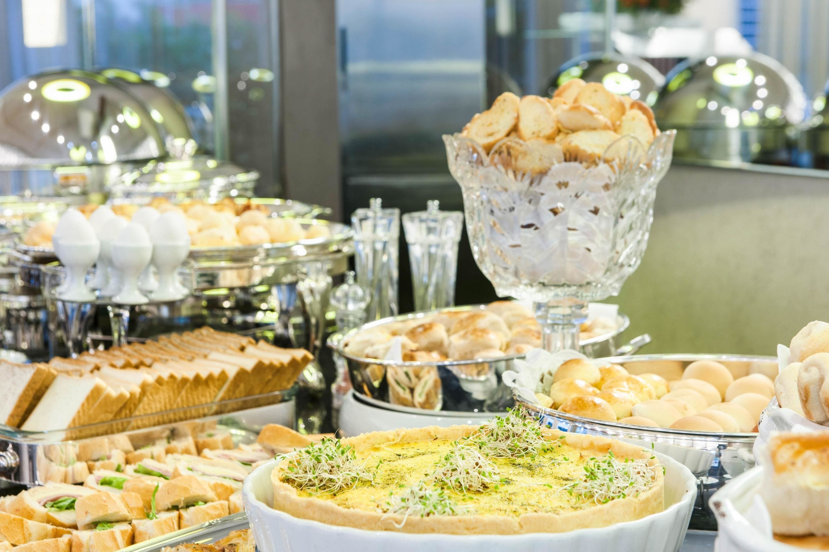 A buffet with various food items including sandwiches, pastries, and a quiche.