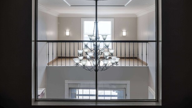 Une vue à travers la fenêtre d’une pièce dotée d’un lustre, d’un balcon et d’un plafond blanc.