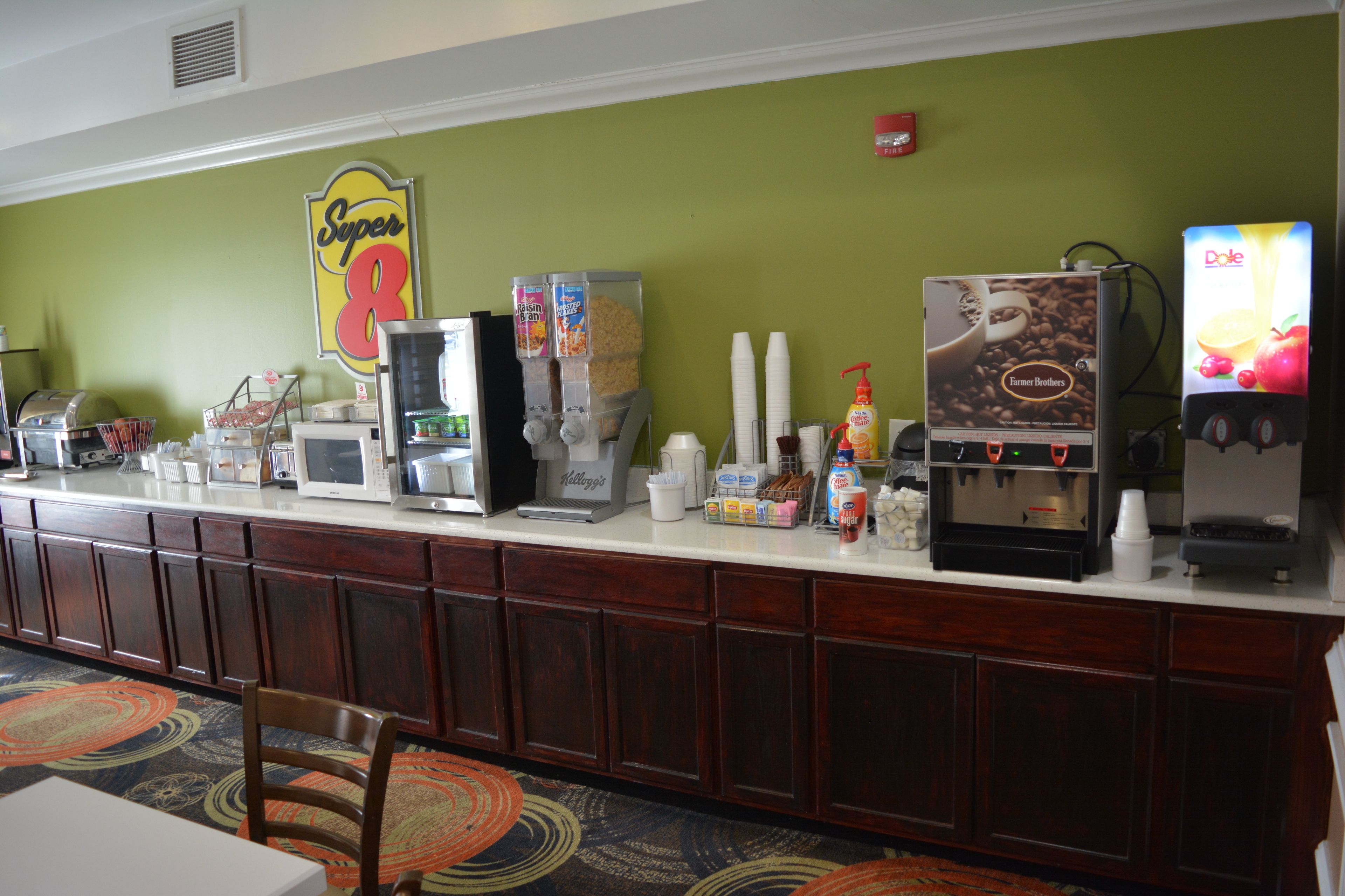 A self-service breakfast bar with various food and drink options, including cereal, coffee, and juice dispensers.