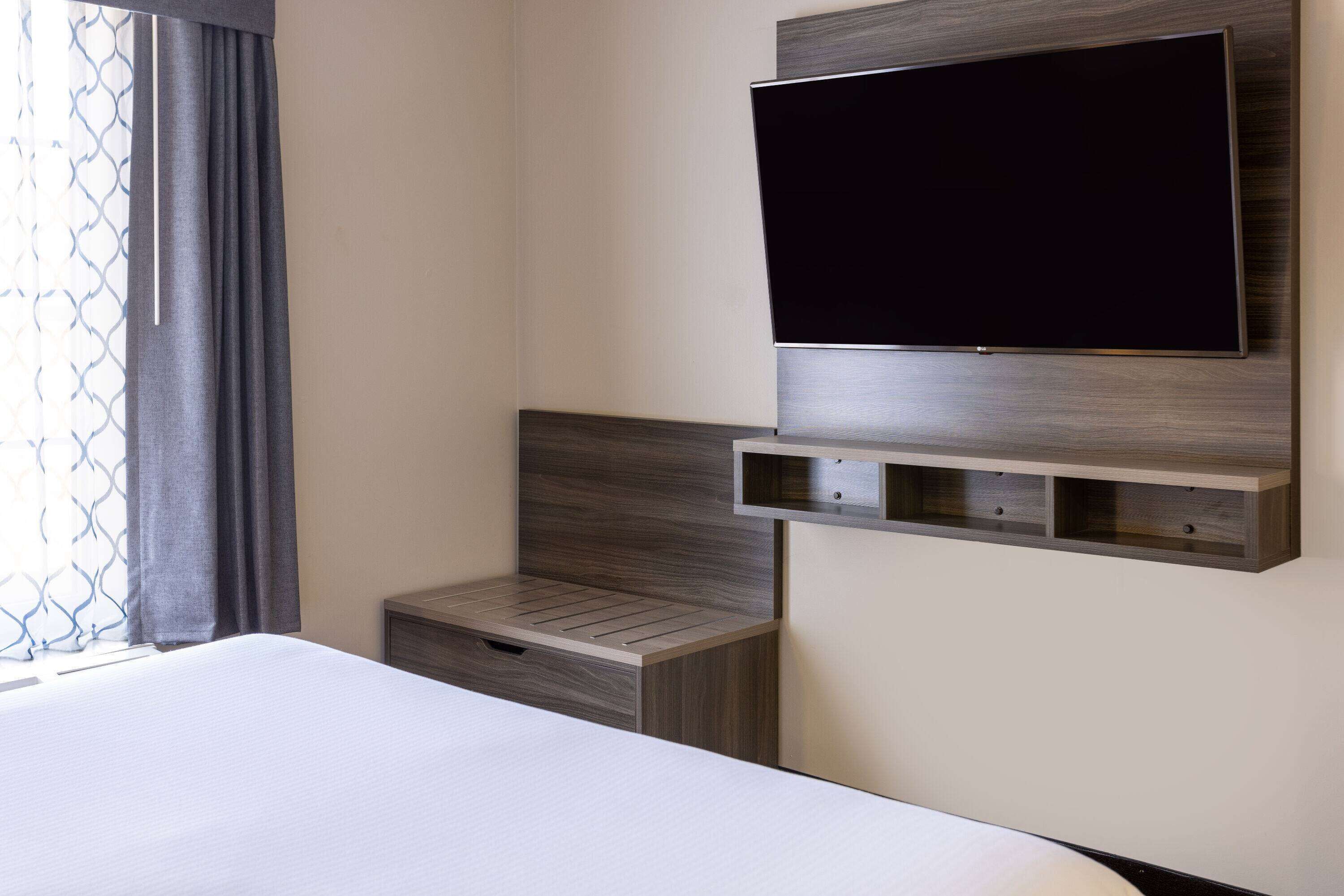A modern hotel room with a large bed, a mounted TV, and built-in storage.