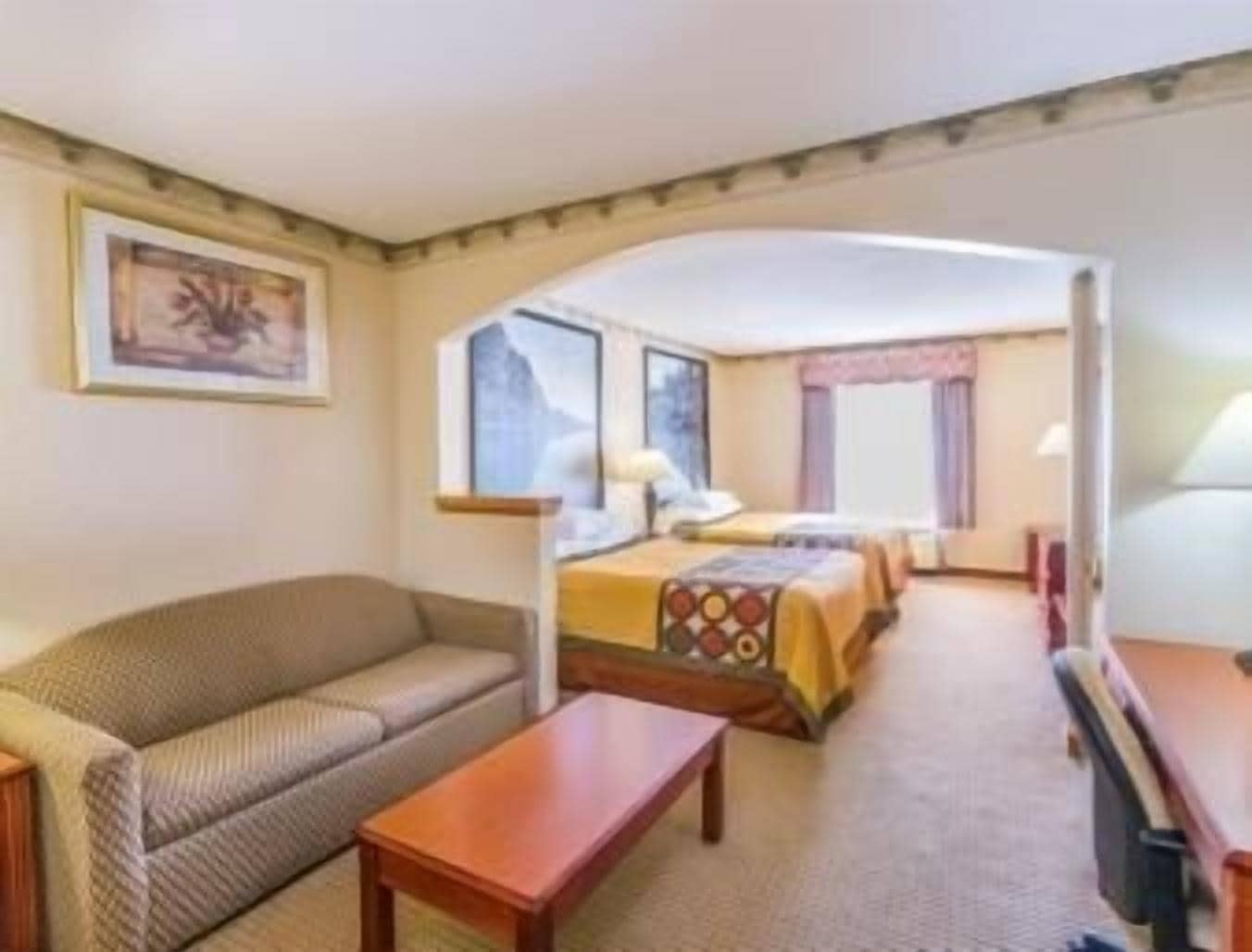 Ein Hotelzimmer mit Sofa, einem kleinen Tisch, einem Bett mit gemustertem Bettbezug, einem Fenster und einem Gemälde an der Wand.