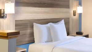 Une chambre d’hôtel avec une tête de lit en bois, du linge de lit blanc et des lampes de chevet.