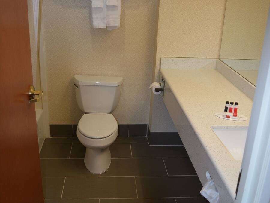 Un baño con inodoro, toallero con toallas, espejo y lavamanos con artículos de aseo.