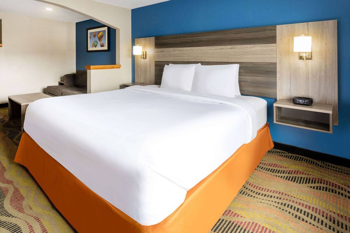 Een hotelkamer met een groot bed, een nachtkastje met een lamp, een bureau en een stoel.