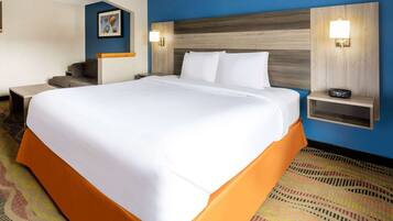 Una habitación de hotel con una cama grande, una mesita de noche con lámpara, un escritorio y una silla.