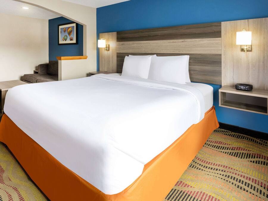 Una habitación de hotel con una cama grande, una mesita de noche con lámpara, un escritorio y una silla.