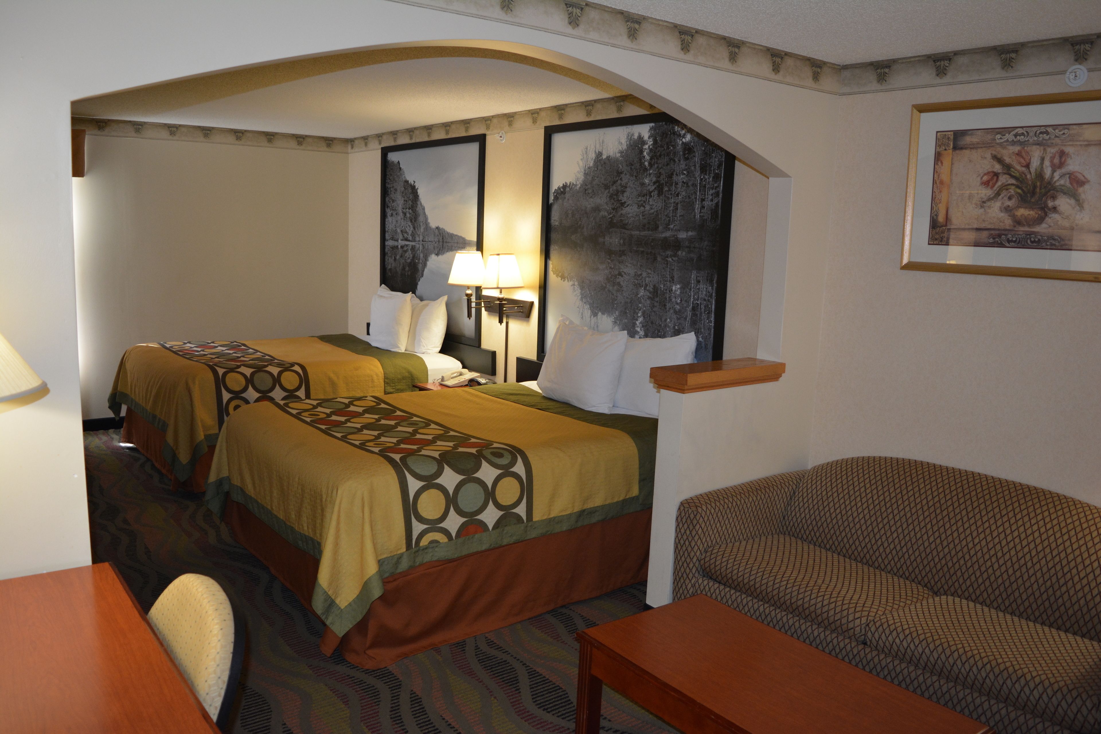 A hotel room with two beds, a sofa, a desk, and a lamp.