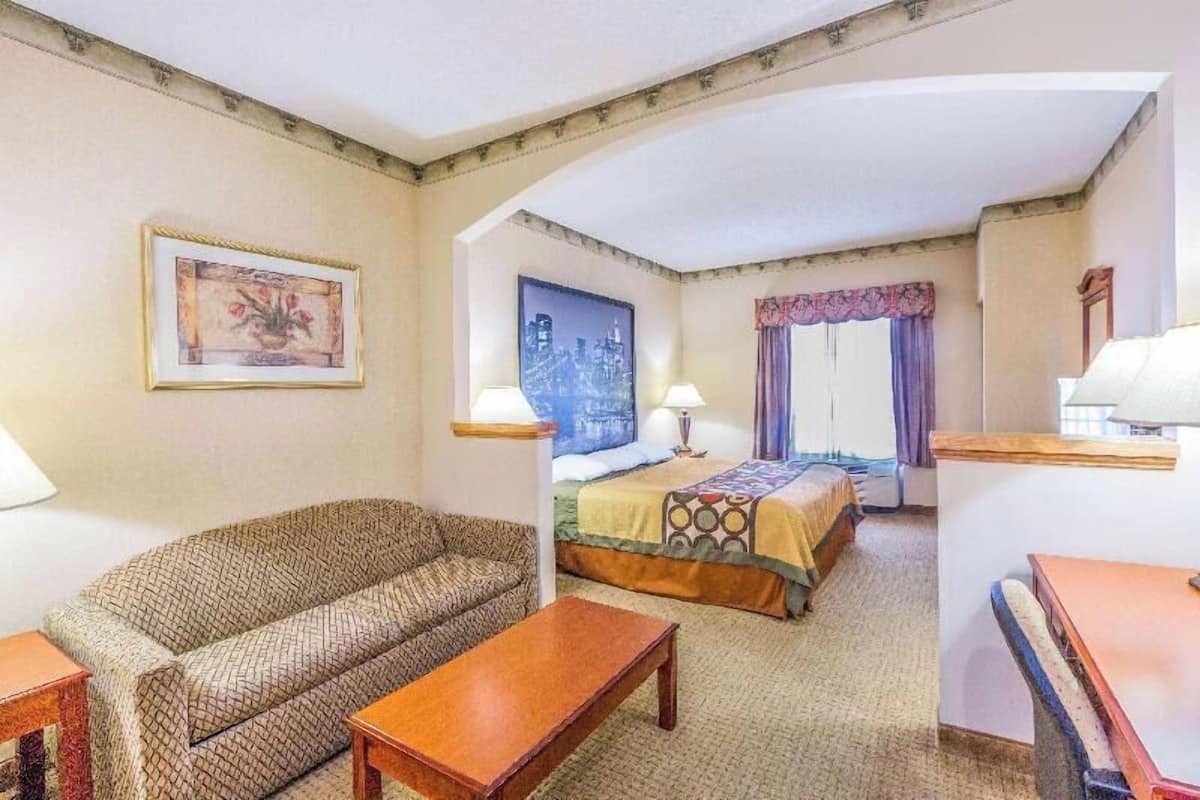 Een hotelkamer met een bank, een bed met een bedovertrek met patroon, een klein tafeltje, een nachtkastje en een ingelijst schilderij aan de muur.