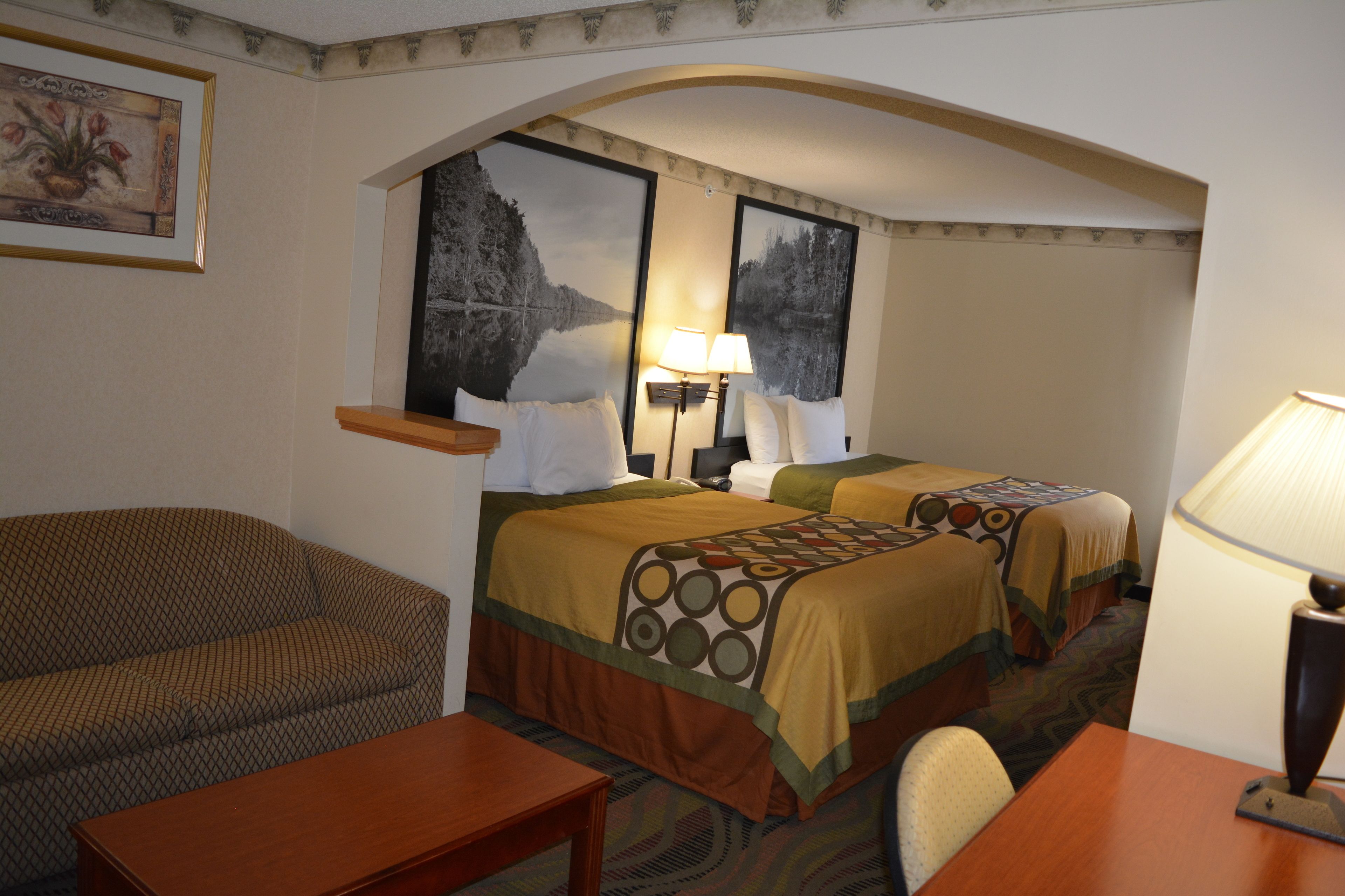 A hotel room with two beds, a sofa, a table, and a lamp.