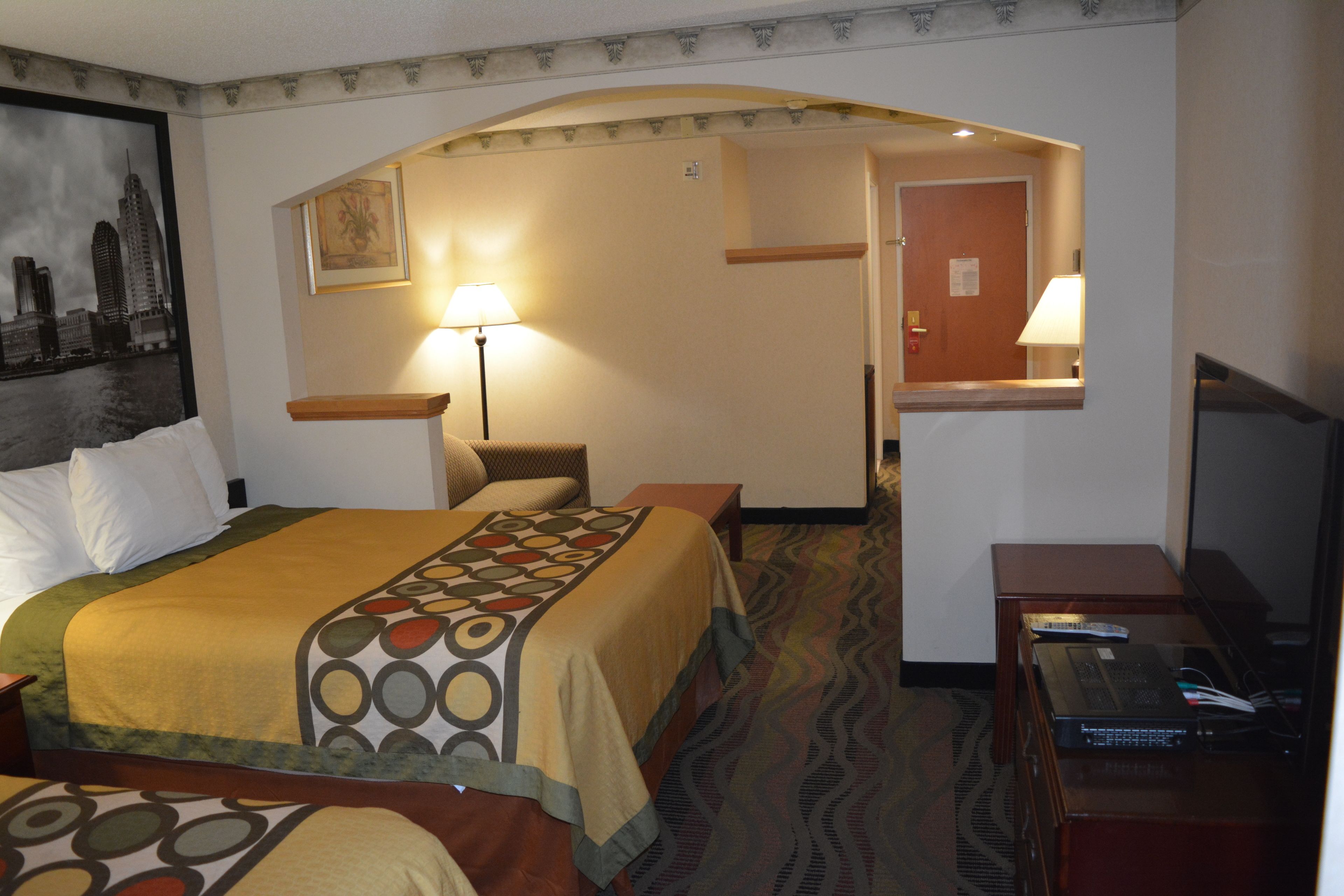 A hotel room with a large bed, a desk with a lamp, a television, and a framed picture on the wall.