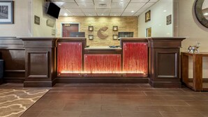 A reception area with a wooden reception desk, a wall-mounted television, and a decorative wall with a crescent moon design. - Comfort Suites Newark - Harrison (Newark)