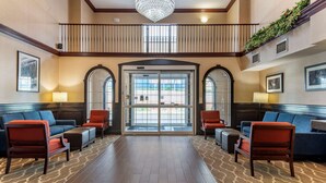 A lobby with a central glass door, two sofas with red cushions, a chandelier, and a patterned rug. - Comfort Suites Newark - Harrison (Newark)