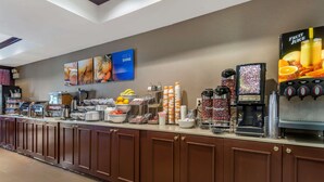 A breakfast bar with a coffee machine, fruit juice dispenser, and various food items. - Comfort Suites Newark - Harrison (Newark)