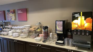 A breakfast bar with coffee machines, a fruit juice dispenser, and various food containers.