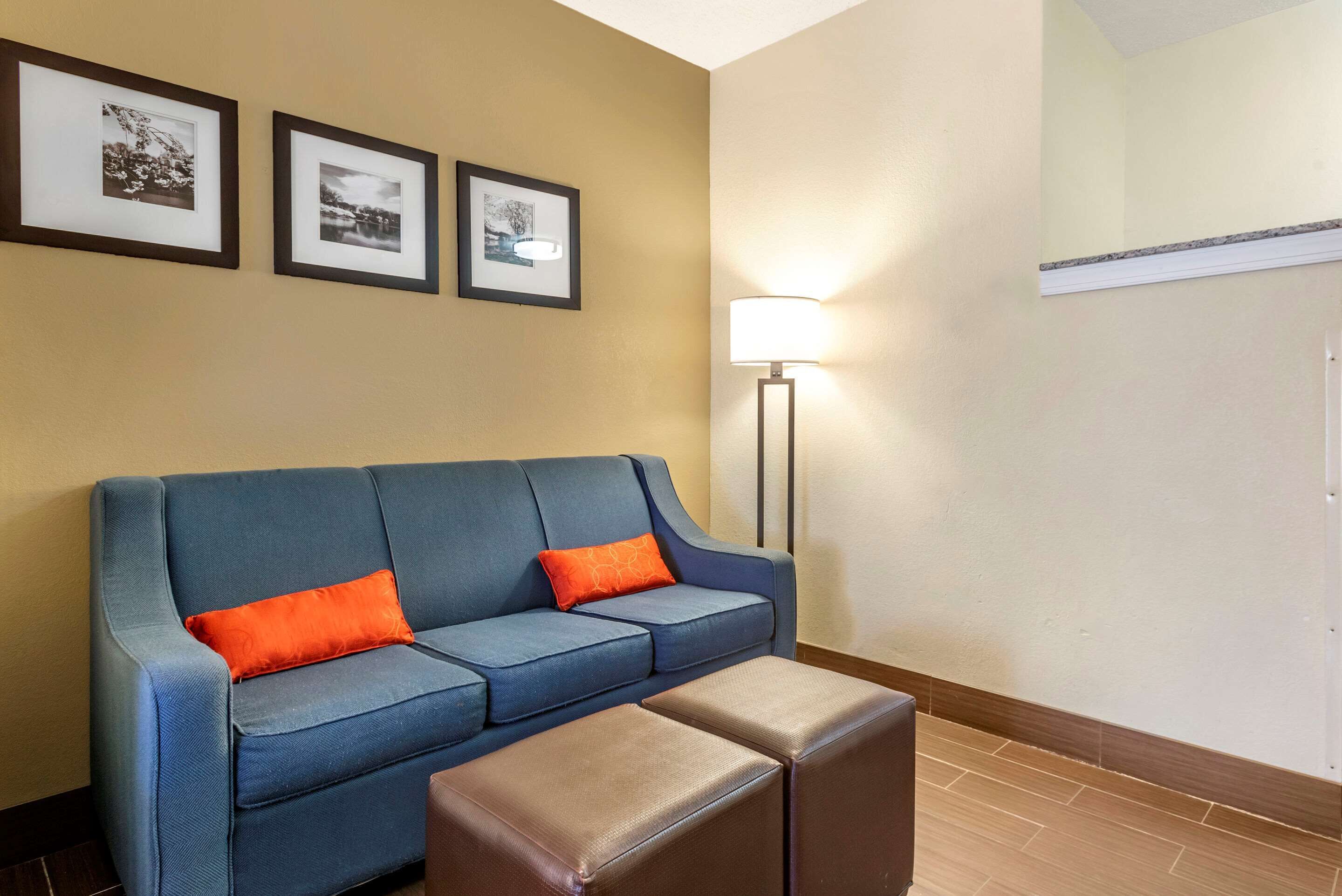 A blue sofa with orange cushions, a small ottoman, and framed pictures on the wall.