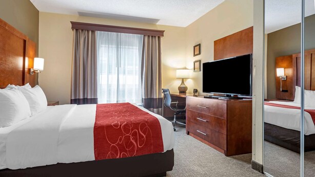 A hotel room with a large bed, a desk with a TV, a chair, and a mirror. - Comfort Suites Newark - Harrison (Newark)