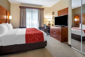 Ein Hotelzimmer mit einem großen Bett, einem Schreibtisch mit Fernseher, einem Sessel und einem Spiegel.
