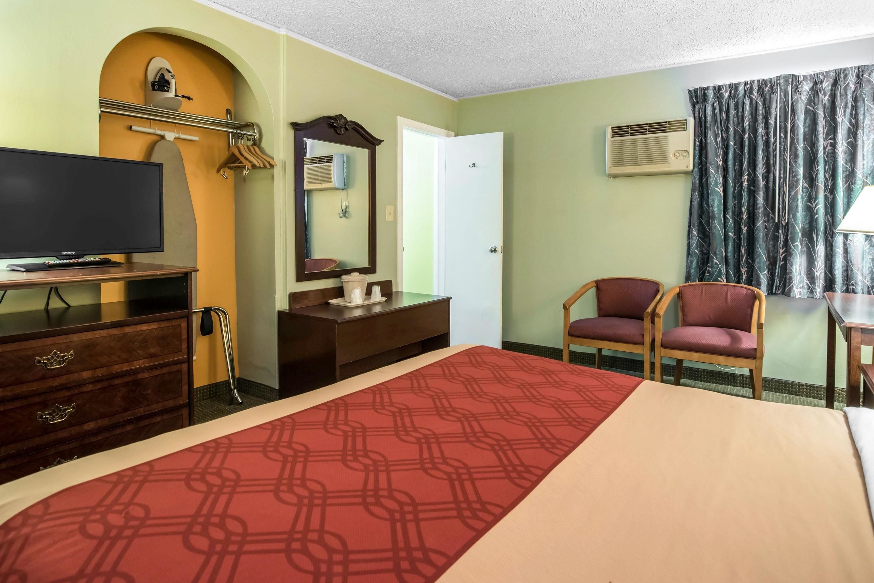 A hotel room with a bed, a TV, a dresser, a mirror, a chair, and a window with curtains.
