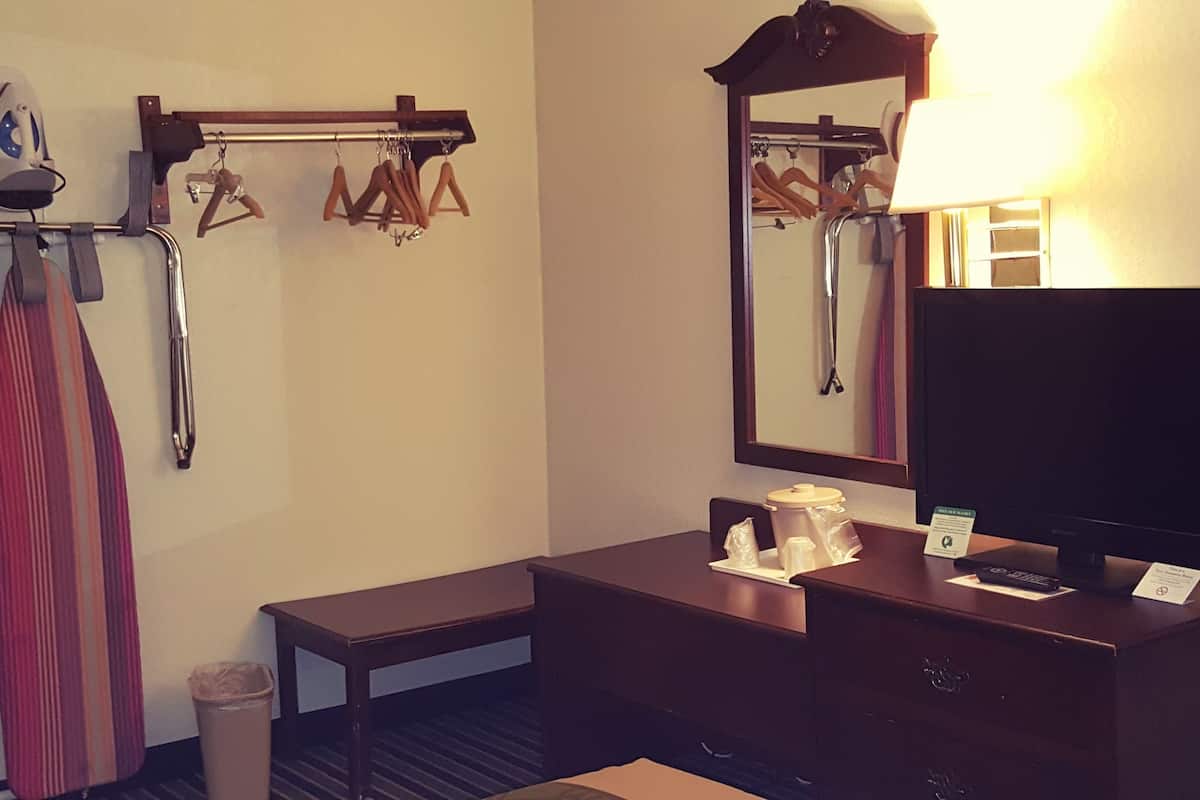 Ein Hotelzimmer mit einem Holzkasten, einem Spiegel, einem Fernseher und einem Kleiderständer mit Kleiderbügeln.