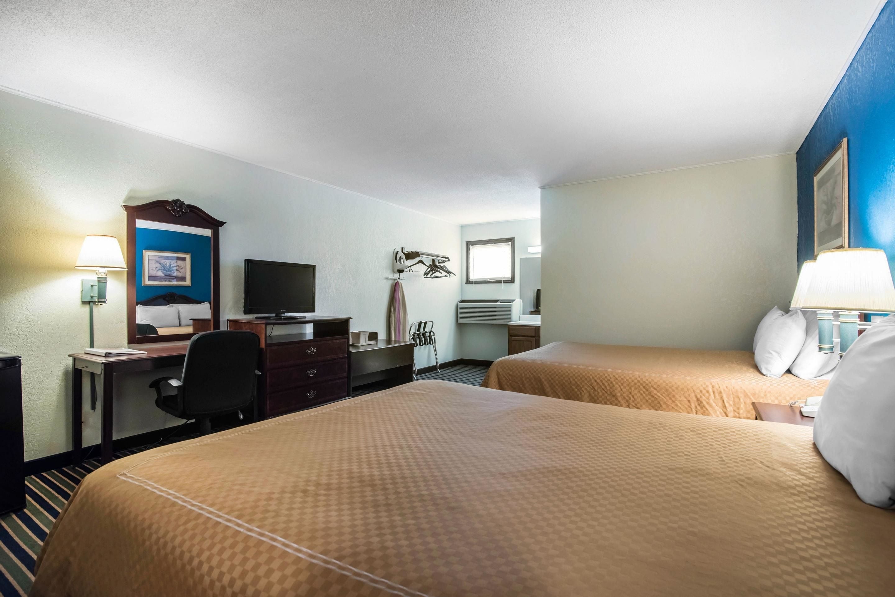 A hotel room with two beds, a desk with a computer, a television, and a window.