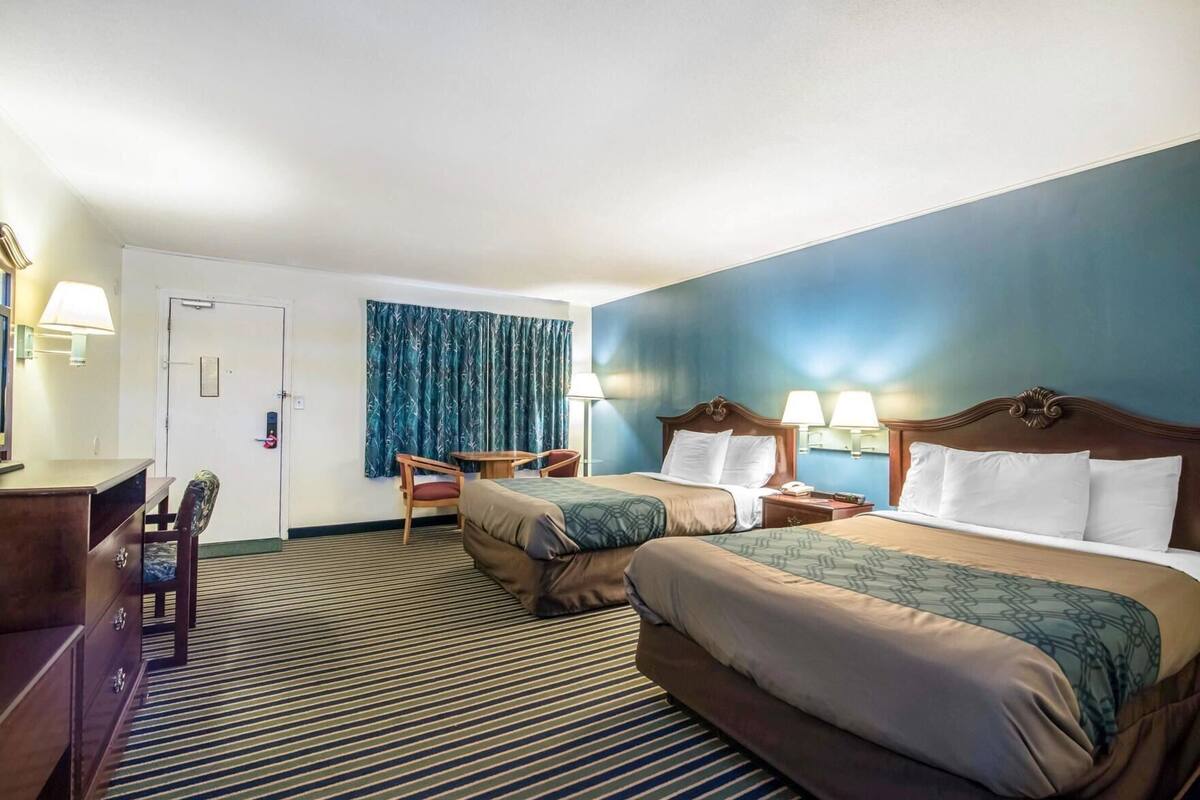 Ein Hotelzimmer mit zwei Betten, einem Schreibtisch, einem Stuhl und einer Tür.