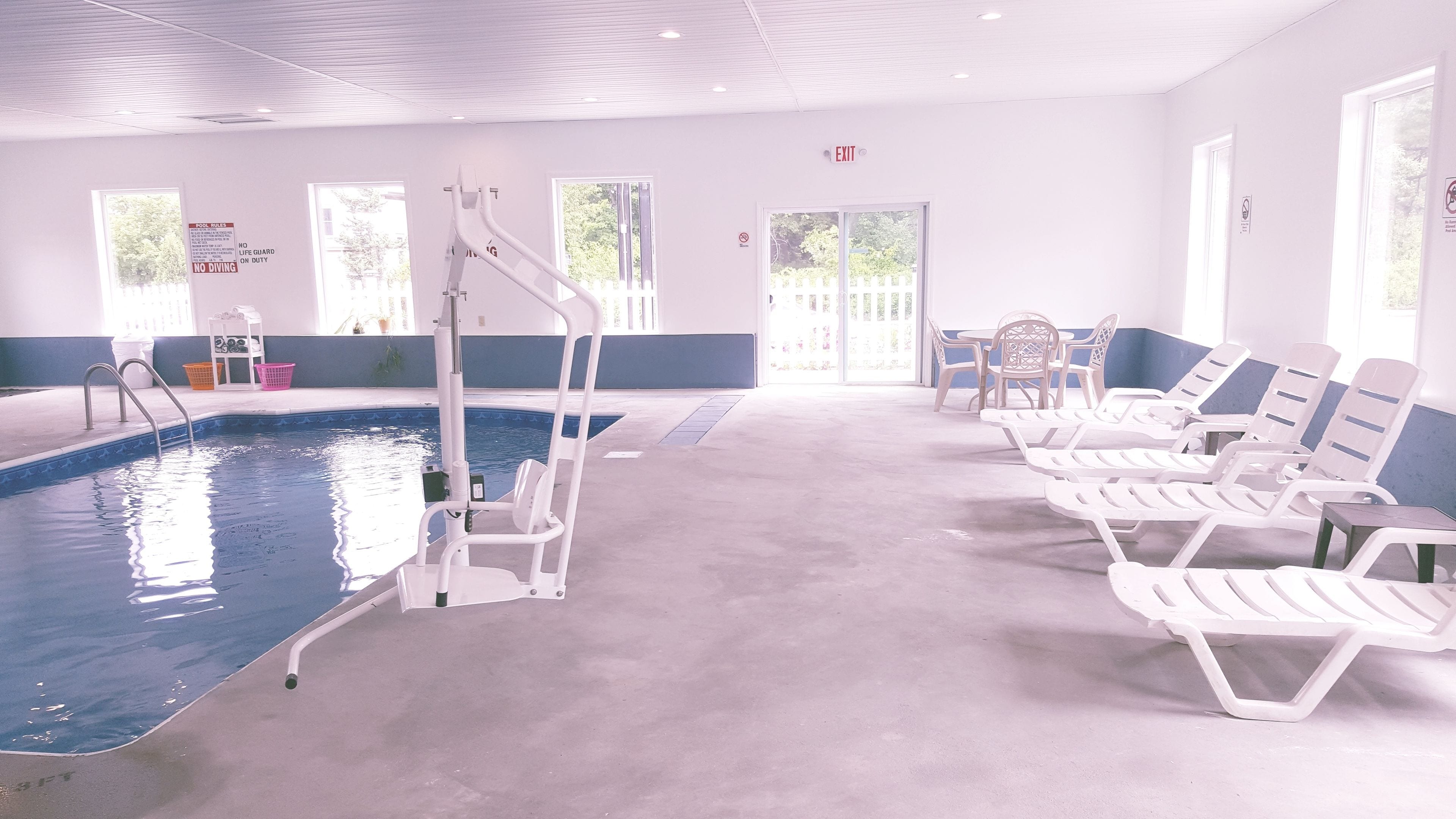 A swimming pool area with a lifeguard stand, lounge chairs, and a clear view of the outdoors through large windows.