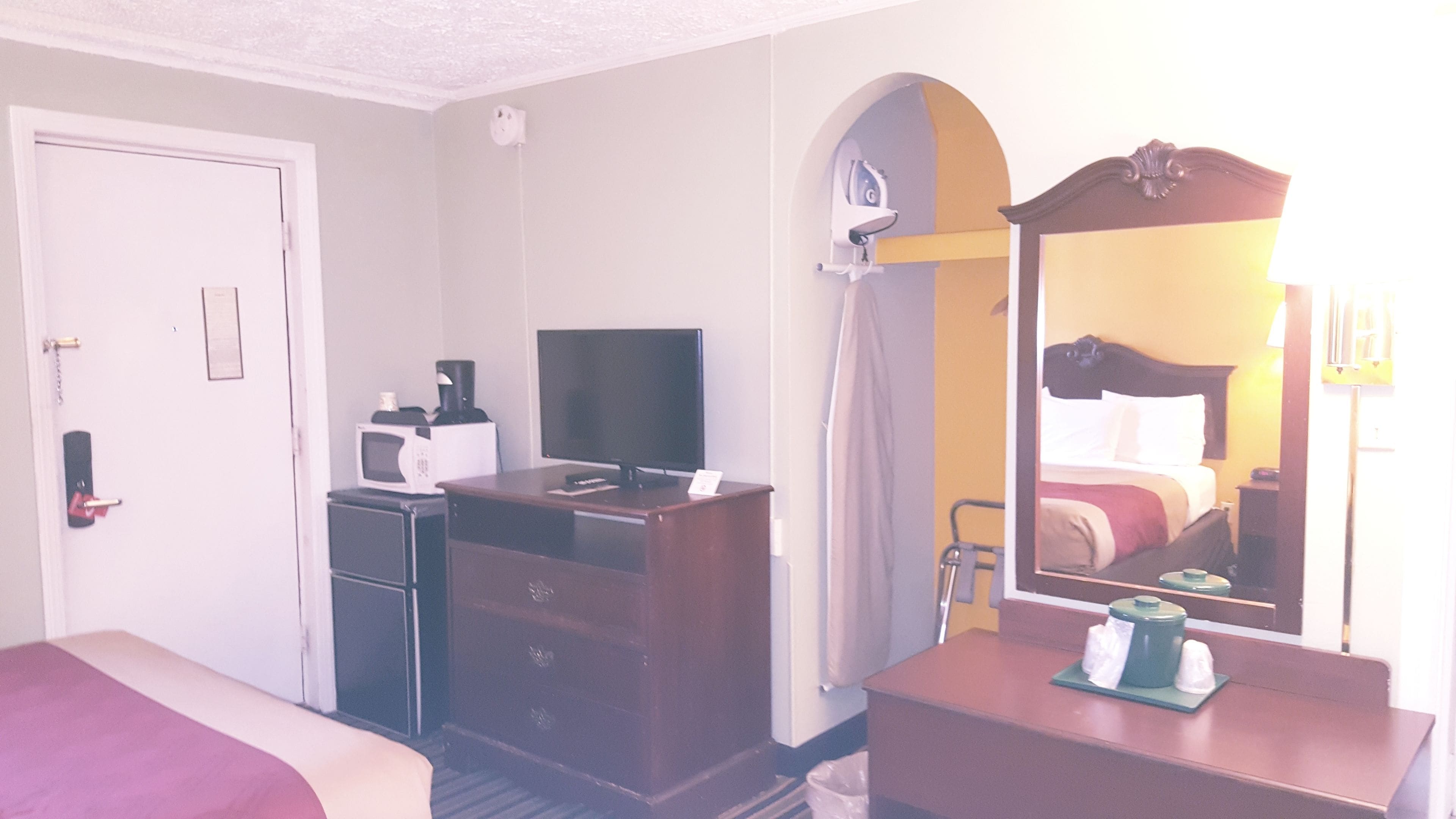 A hotel room with a bed, a desk with a computer, a television, a microwave, and a dresser.