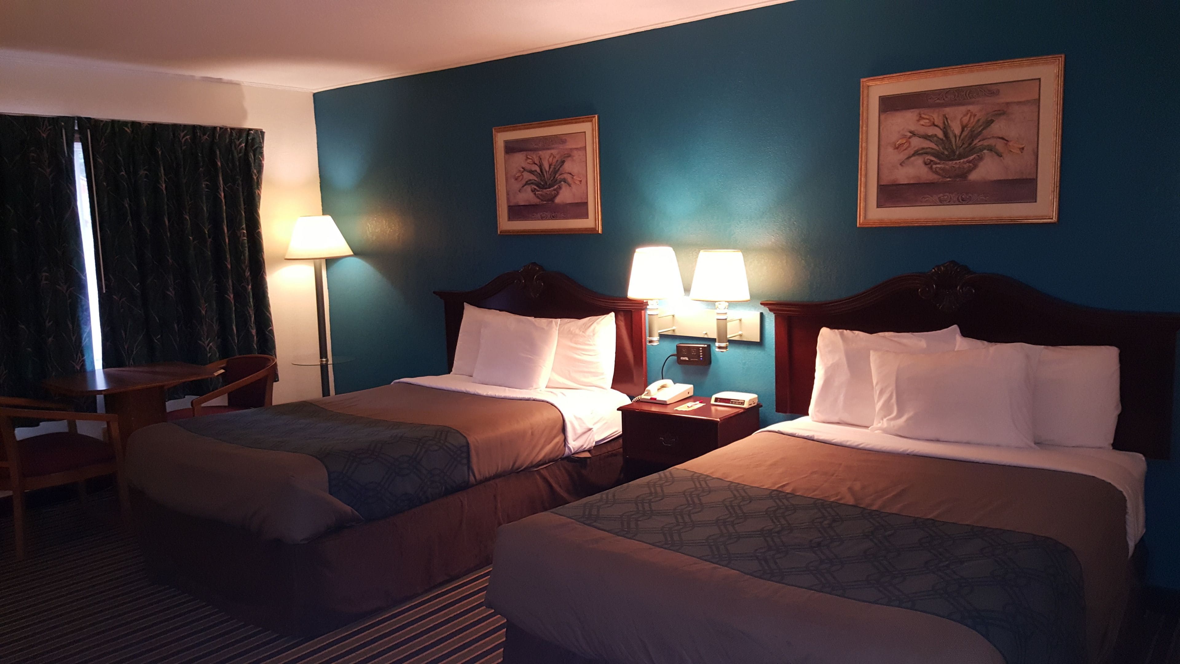 A hotel room with two beds, a desk, a chair, and two lamps.