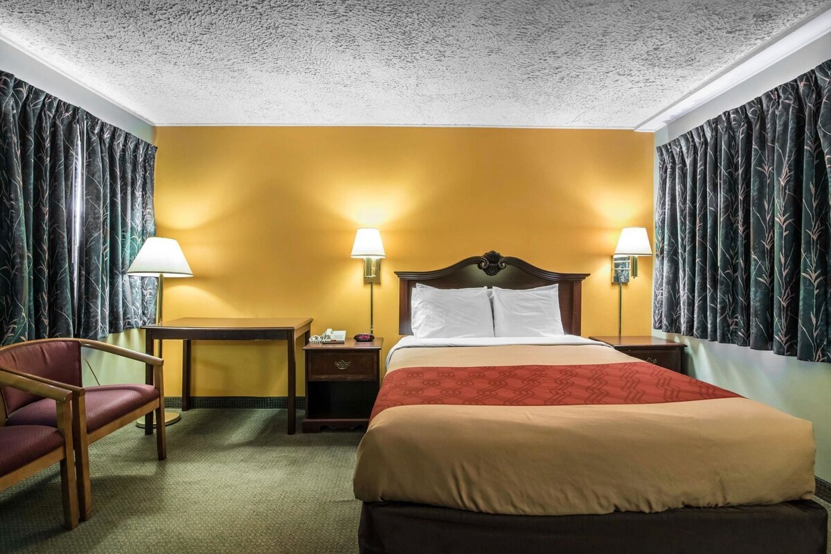 Ein Hotelzimmer mit einem Bett, zwei Nachttischen, einem Sessel und einer Lampe.