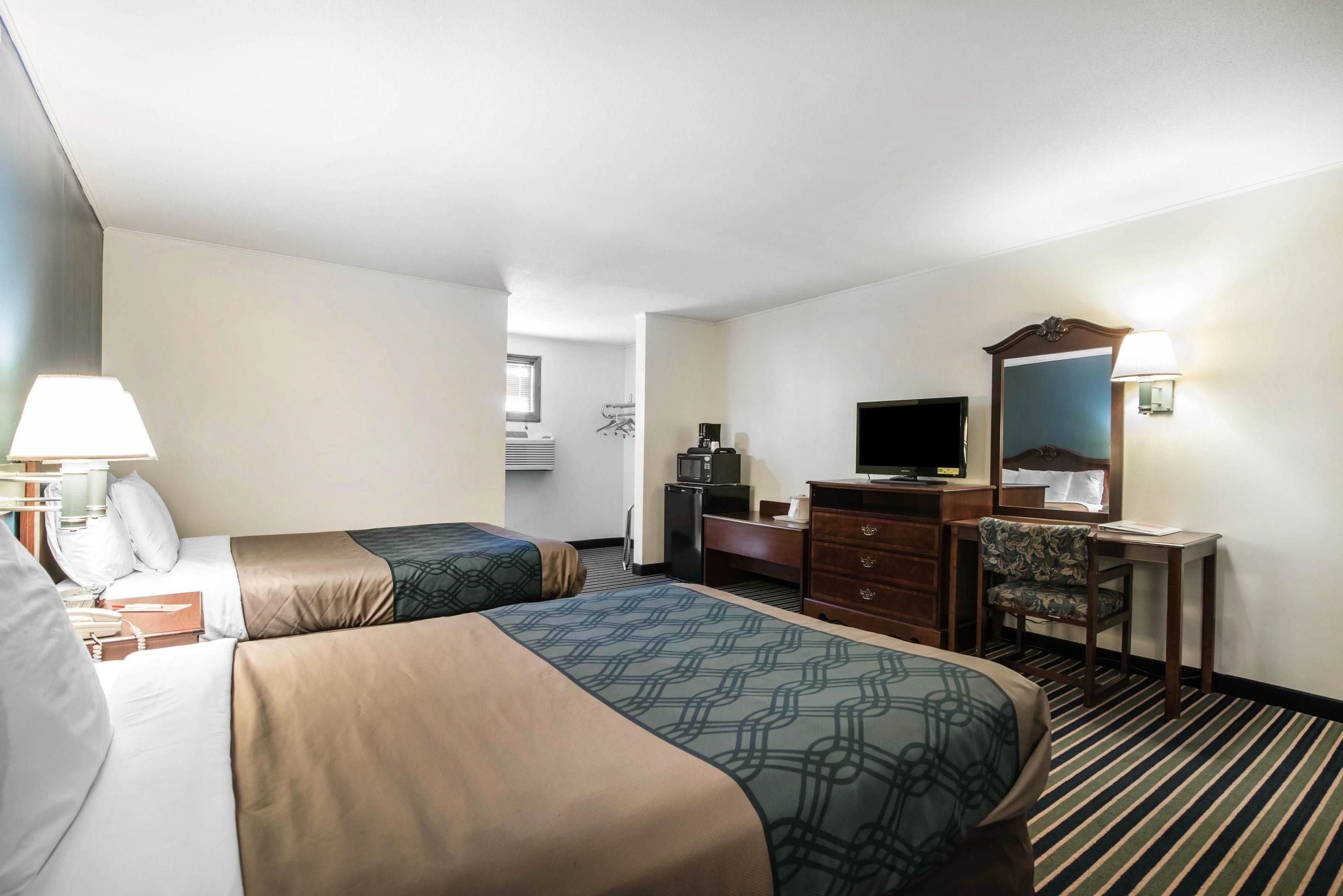 A hotel room with two beds, a desk, a television, a dresser, and a mirror.
