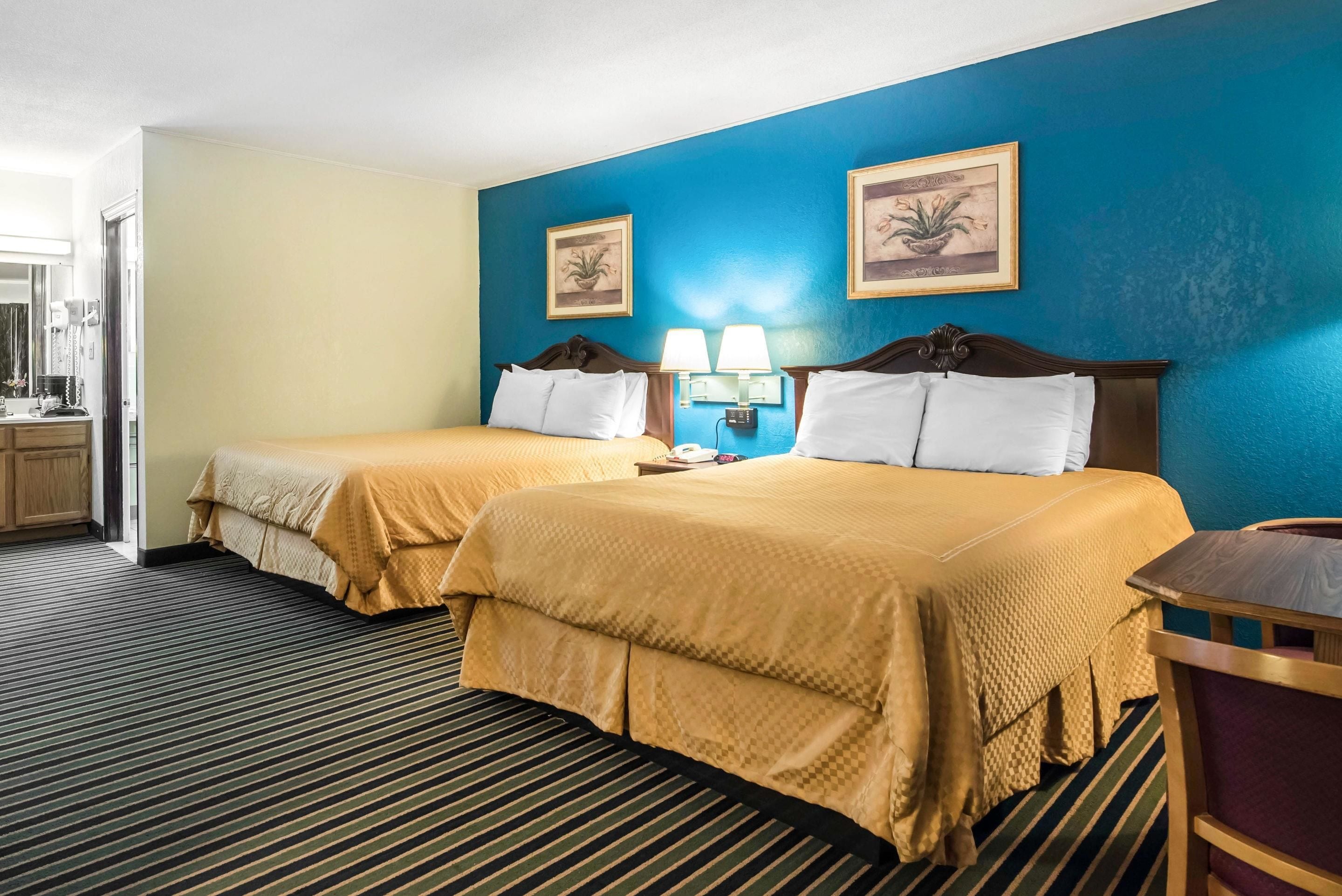 A hotel room with two beds, a bathroom, and a desk with a chair.