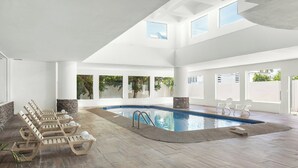 A spacious indoor swimming pool area with multiple lounge chairs and a clear view of the outside through large windows. - Fiesta Inn Express Hermosillo (Hermosillo)