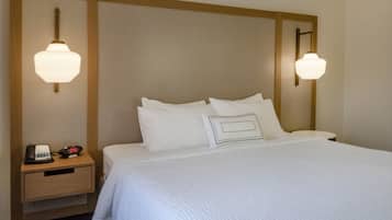 Ein Hotelzimmer mit einem großen Bett, zwei Nachttischlampen, einem Nachttisch mit Telefon und Wecker und einem hölzernen Kopfteil.