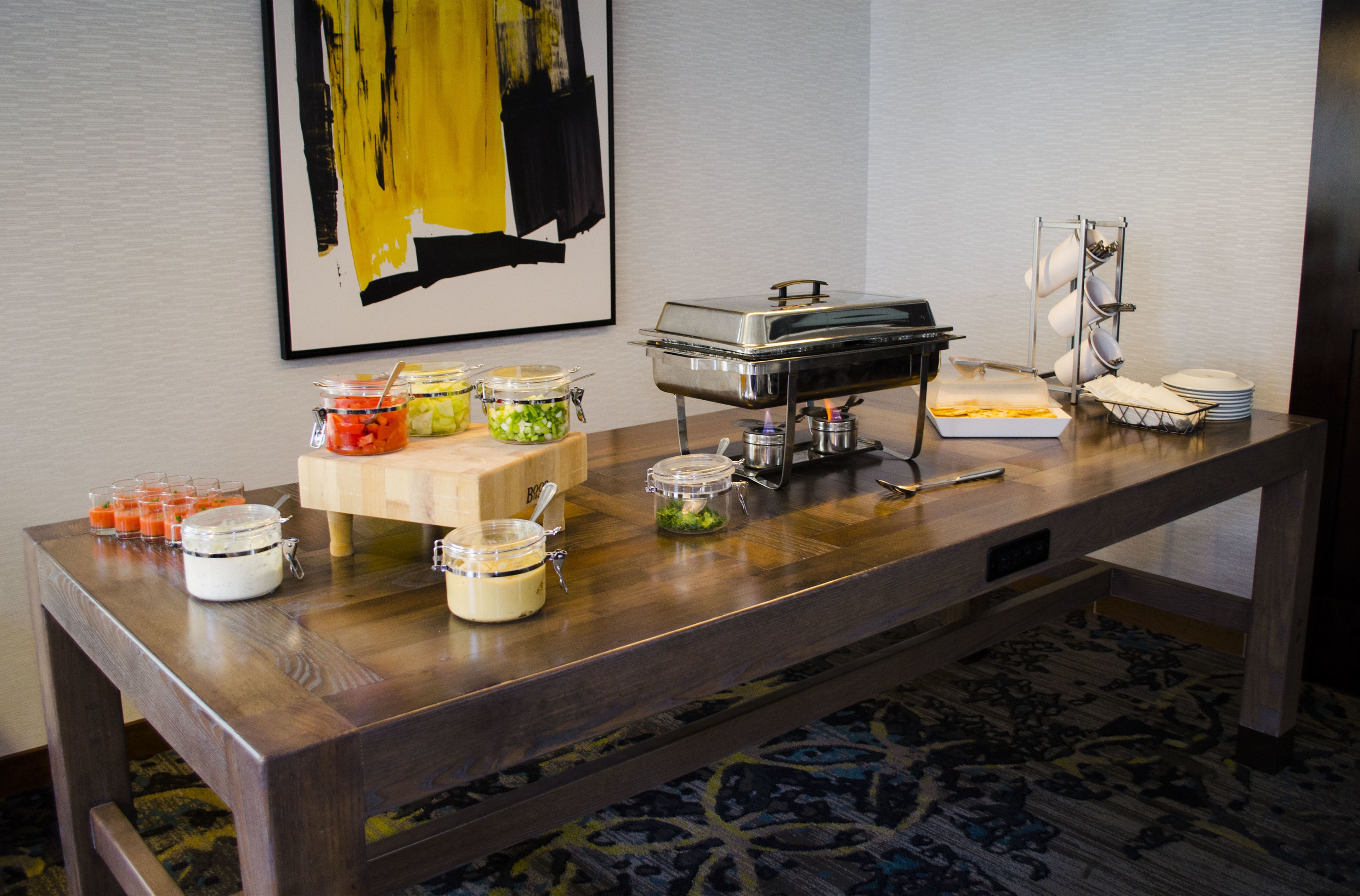 Una mesa de buffet con varios recipientes de comida, una estación de alimentos calientes de autoservicio y una pila de platos.