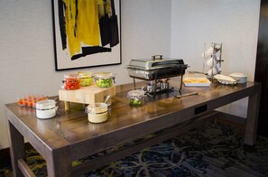 A buffet table with various food containers, a self-service hot food station, and a stack of plates.