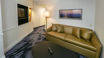Ein Hotelzimmer mit einer Couch, einer Fernbedienung auf einem kleinen Tisch, einer Lampe und einem Fernseher auf einem Schrank.