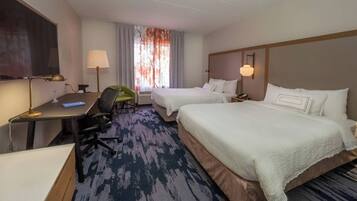 Een hotelkamer met twee bedden, een bureau met stoel, een televisie en een raam met gordijnen.