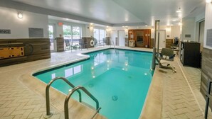 Una piscina interior con suelo de baldosas, una silla de socorrista y señalización del área de la piscina.