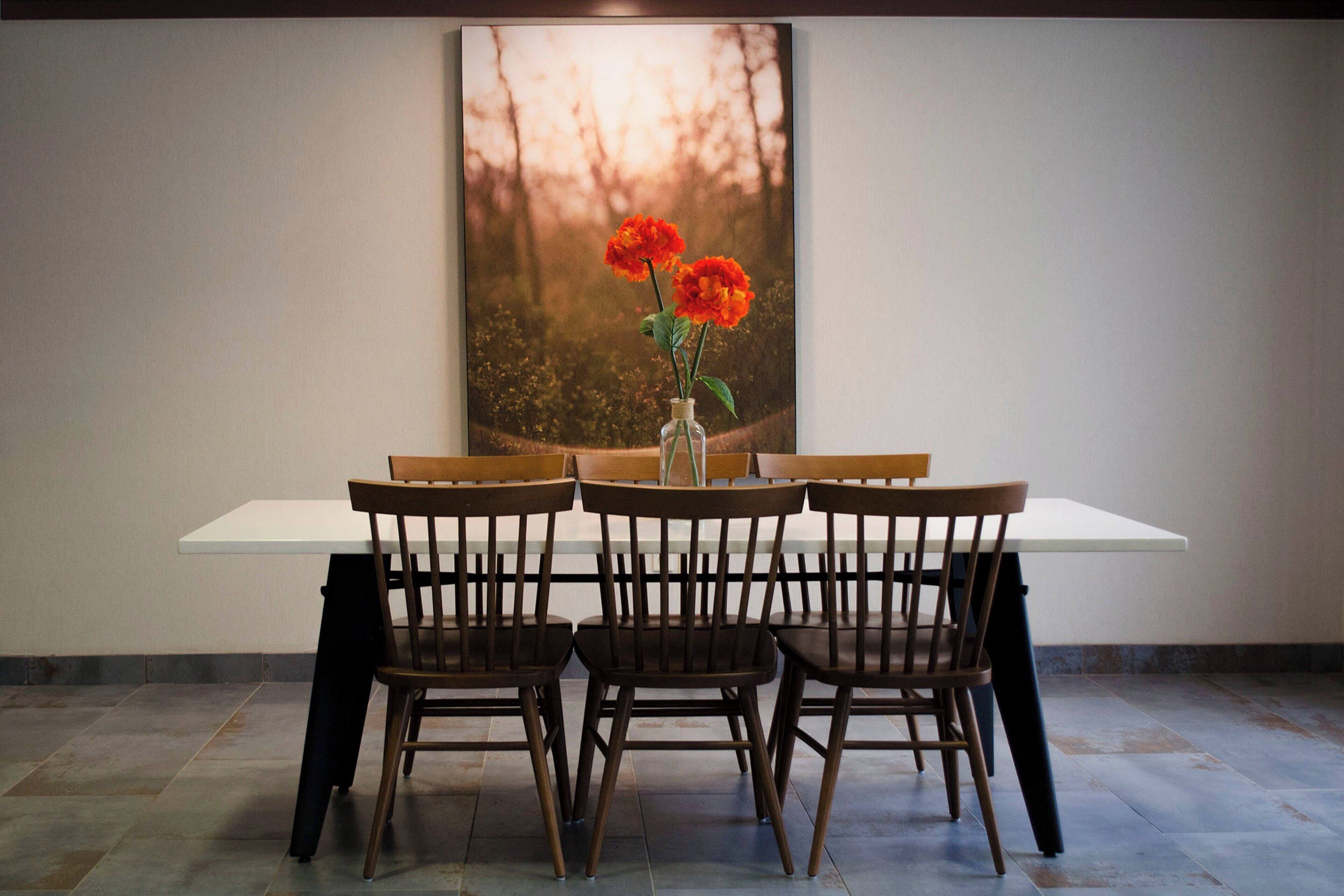 Un comedor con una mesa blanca y sillas de madera, un florero con flores y un cuadro grande en la pared.