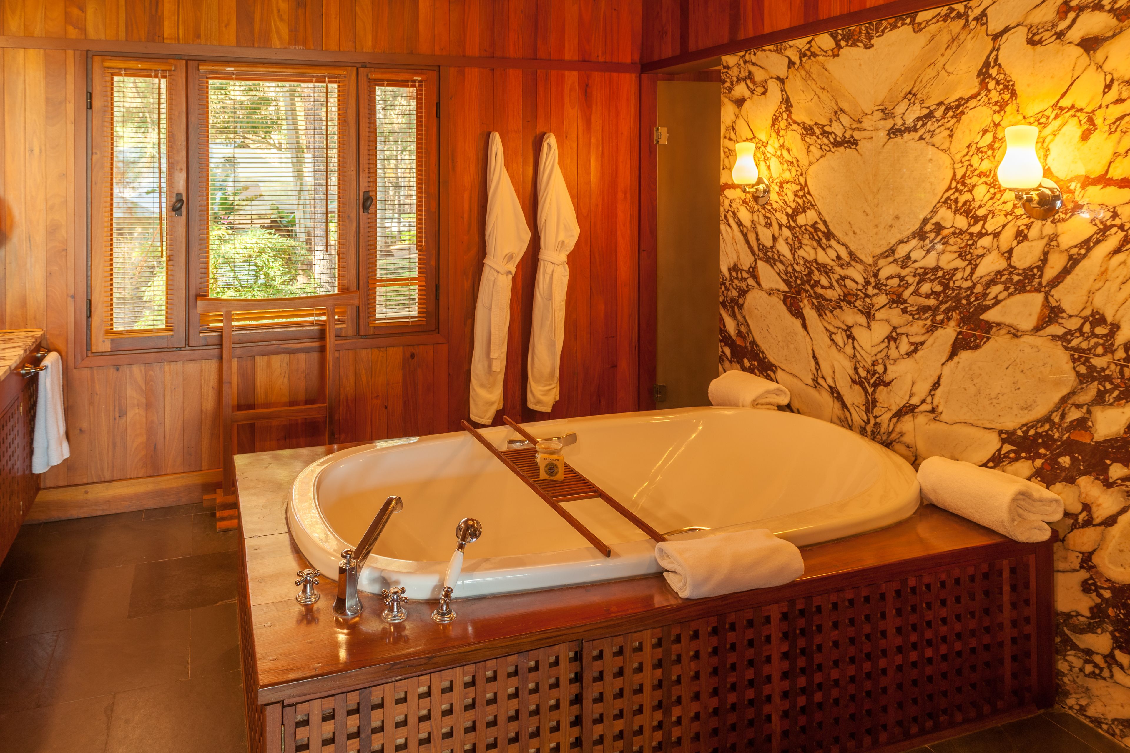 A wooden bathroom with a large bathtub, wooden cabinets, and a stone wall with a heart design.