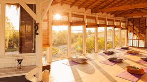 Ein Zimmer mit großen Fenstern, Holzbalken und Yogamatten.