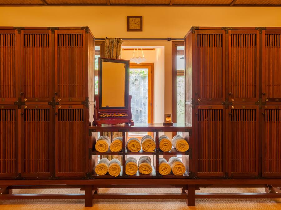 A traditional Japanese room with sliding doors, a wooden bench, and neatly rolled towels.