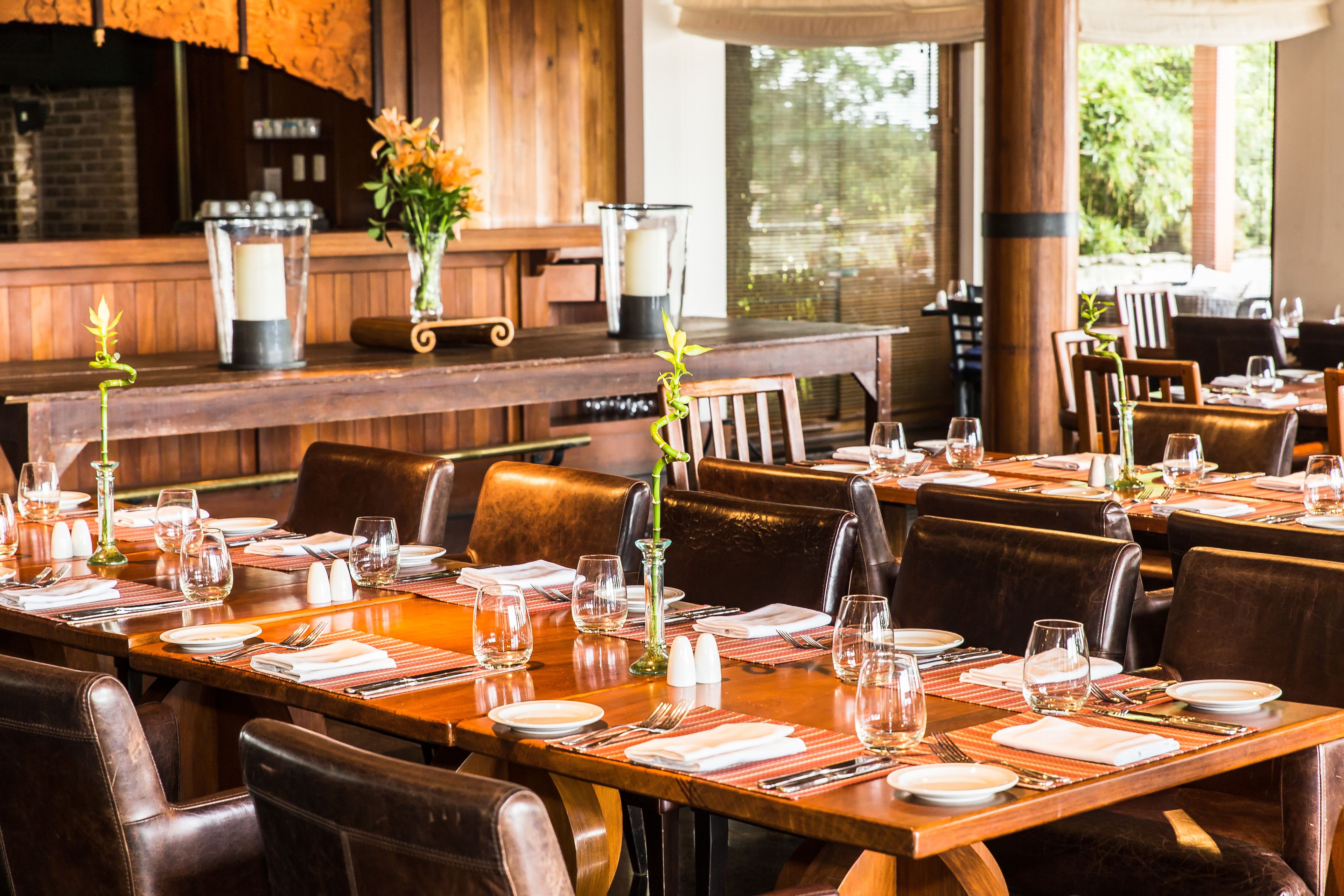 A restaurant with wooden tables and chairs, set with white plates, glasses, and cutlery.