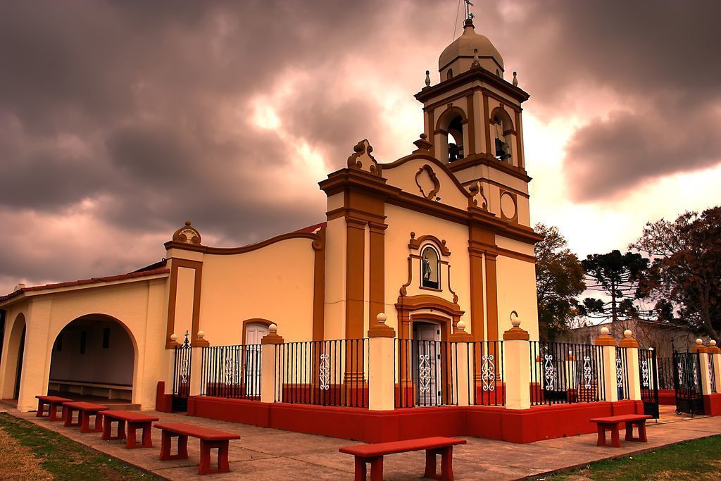 A church with a bell tower, red benches, and a fence.