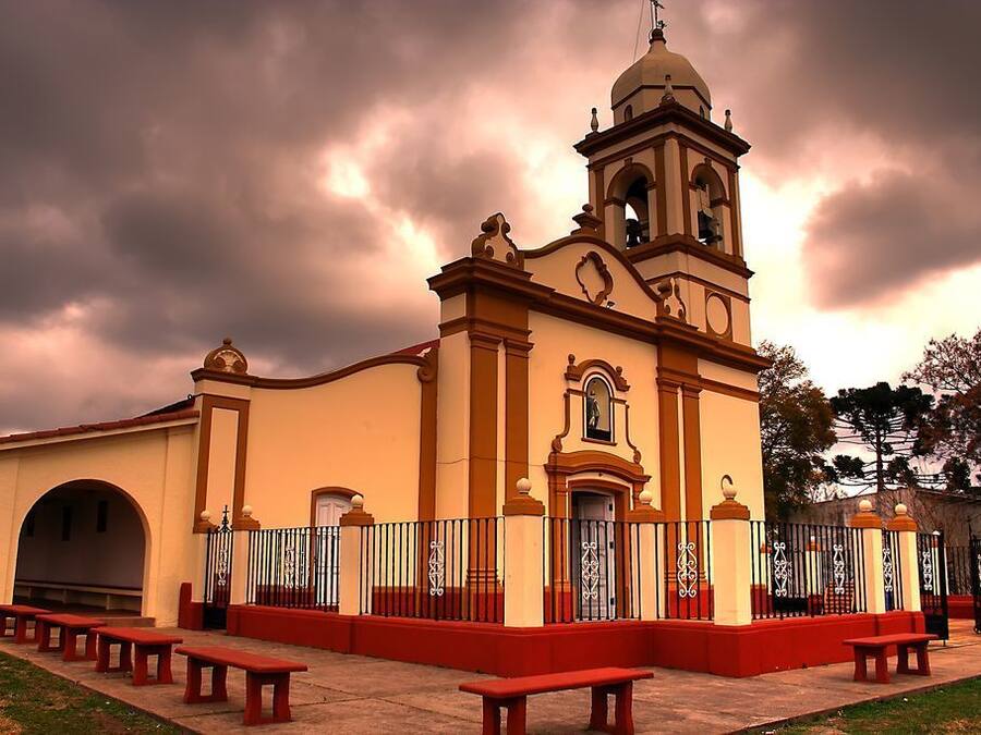 A church with a bell tower, red benches, and a fence.