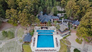 Luftaufnahme eines Resorts mit einem großen zentralen Pool, Gästevillen und umliegenden Grünflächen.