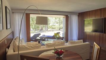 Una habitación moderna con sofá, una mesa de comedor con un jarrón de flores, un televisor montado en la pared y vistas al exterior.