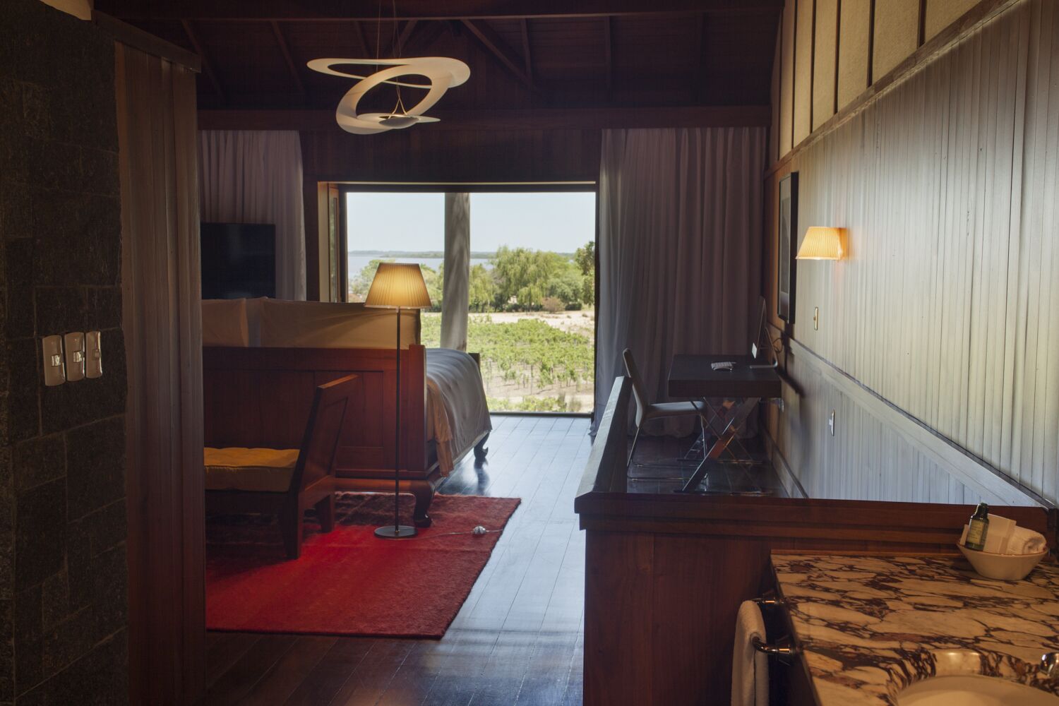 Ein Schlafzimmer mit großem Fenster, einem Bett, einem Schreibtisch und einem Sessel.