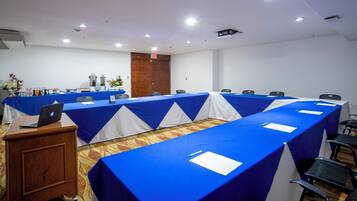 Un salón de conferencias con una larga mesa cubierta con manteles azul y blanco, equipado con sillas, un atril y una computadora portátil.